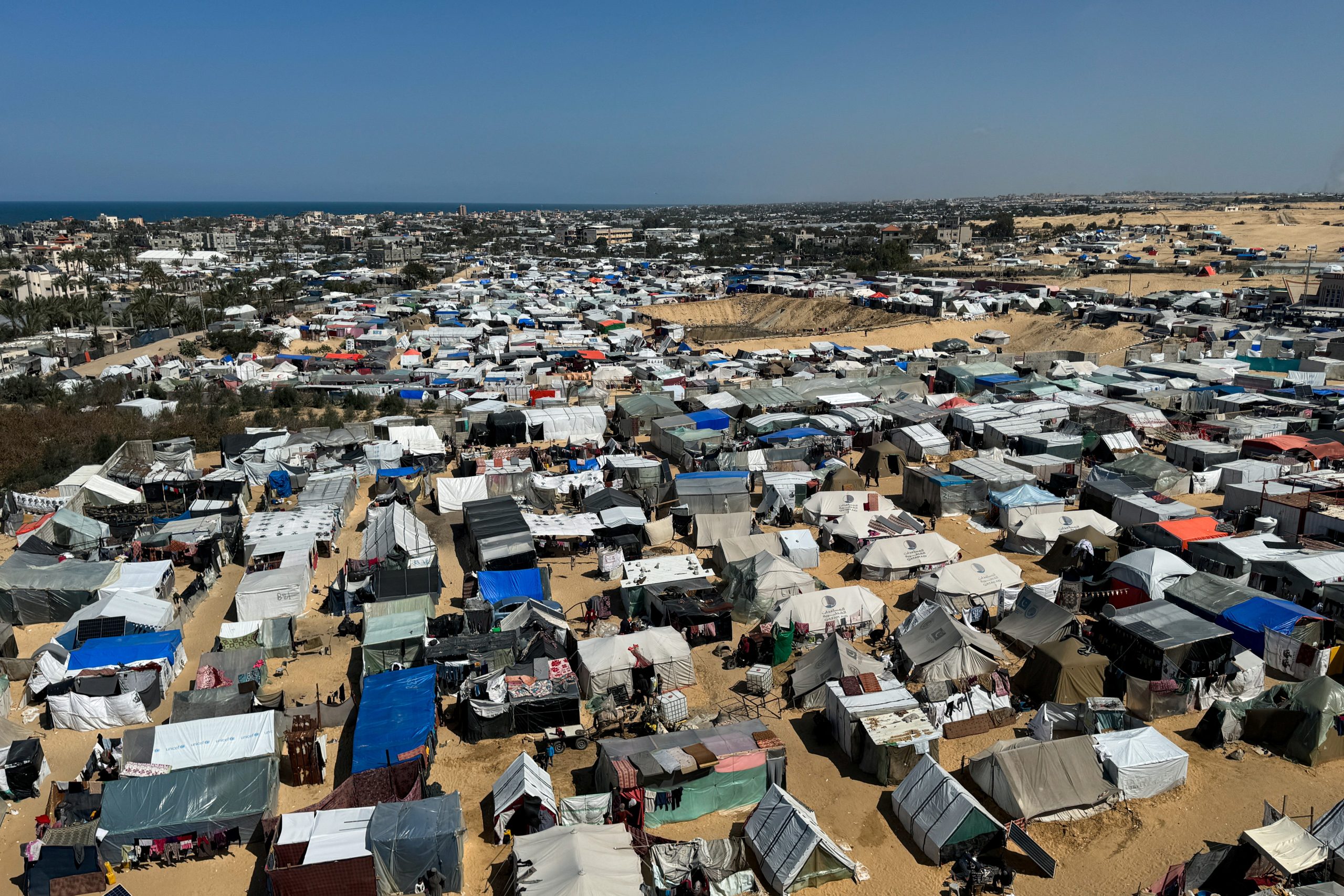 Aerial view of a sprawling displacement tent camp along the coast